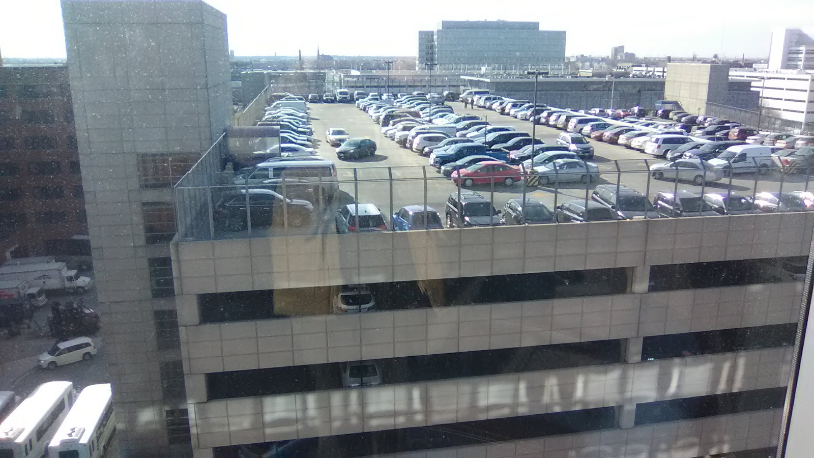 Elevated view of multi-level parking garage with rows of parked vehicles and urban cityscape in background