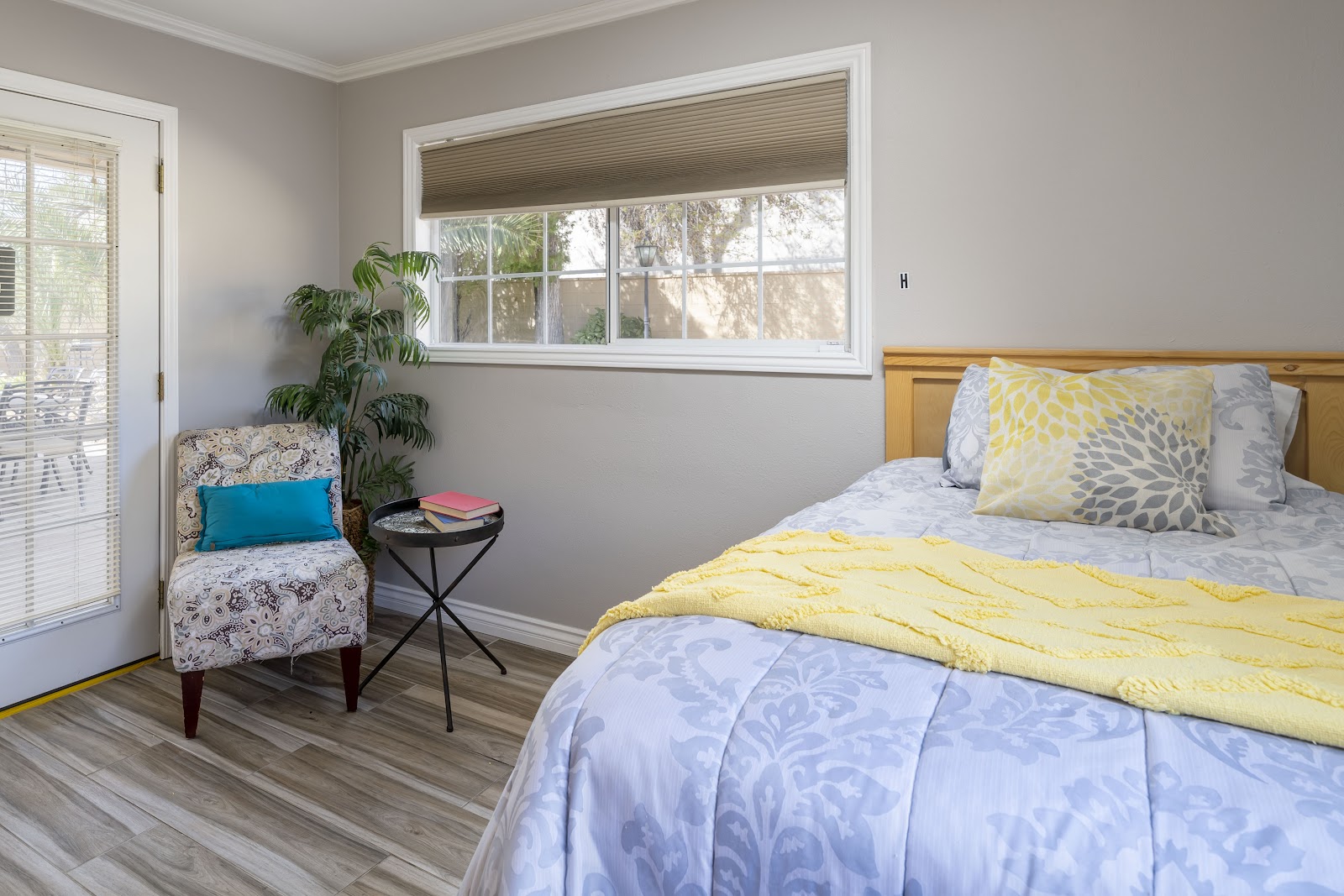 Interior bedroom with queen bed, decorative bedding, upholstered armchair, small accent table, and sliding glass door overlooking grounds.