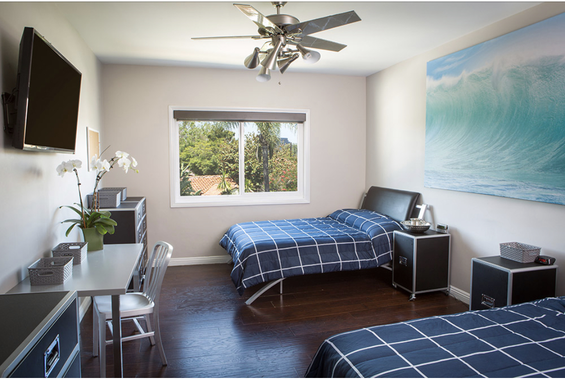 Interior bedroom with two beds, blue bedding, desk, TV, window with outside view, and contemporary furnishings