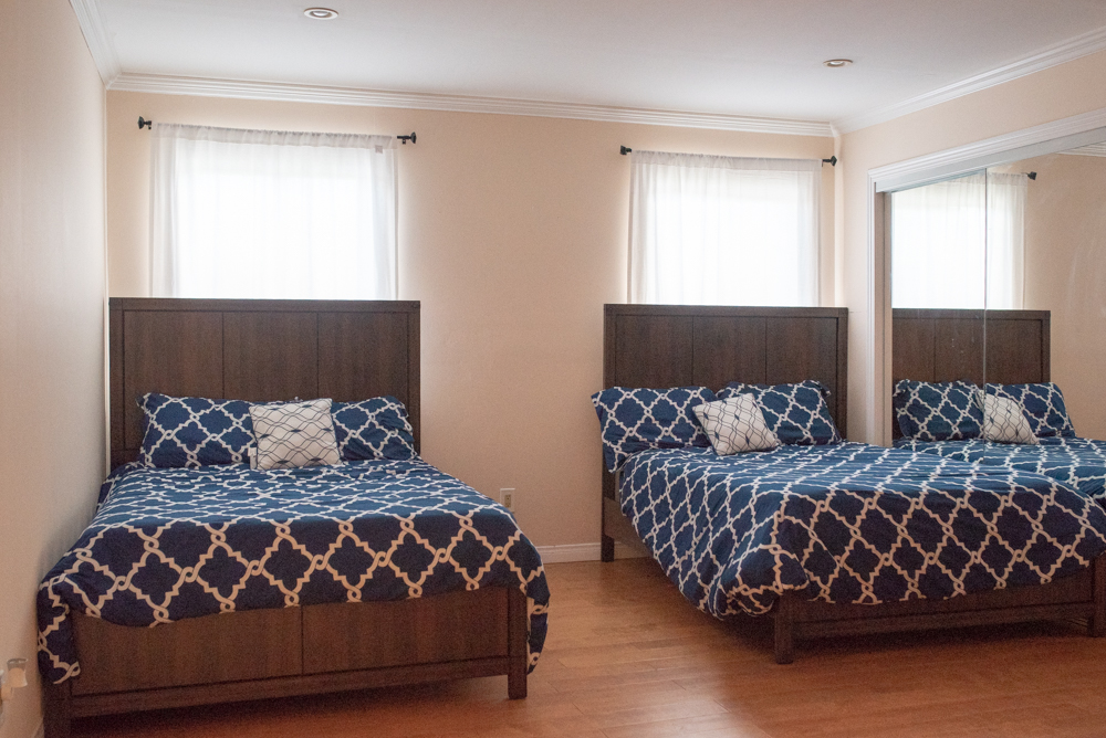 Interior bedroom with two queen beds, wooden headboards, blue patterned bedding, and windows with natural light
