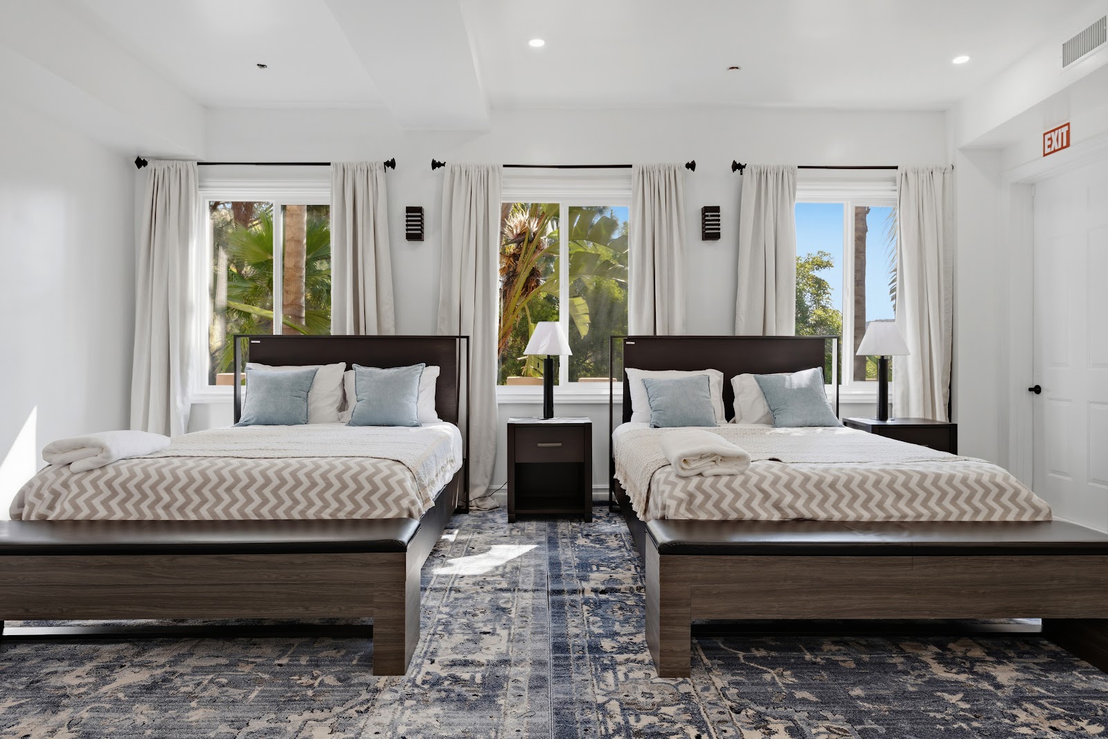 Interior bedroom with two queen beds, black headboards, white bedding, windows with natural light, and modern amenities