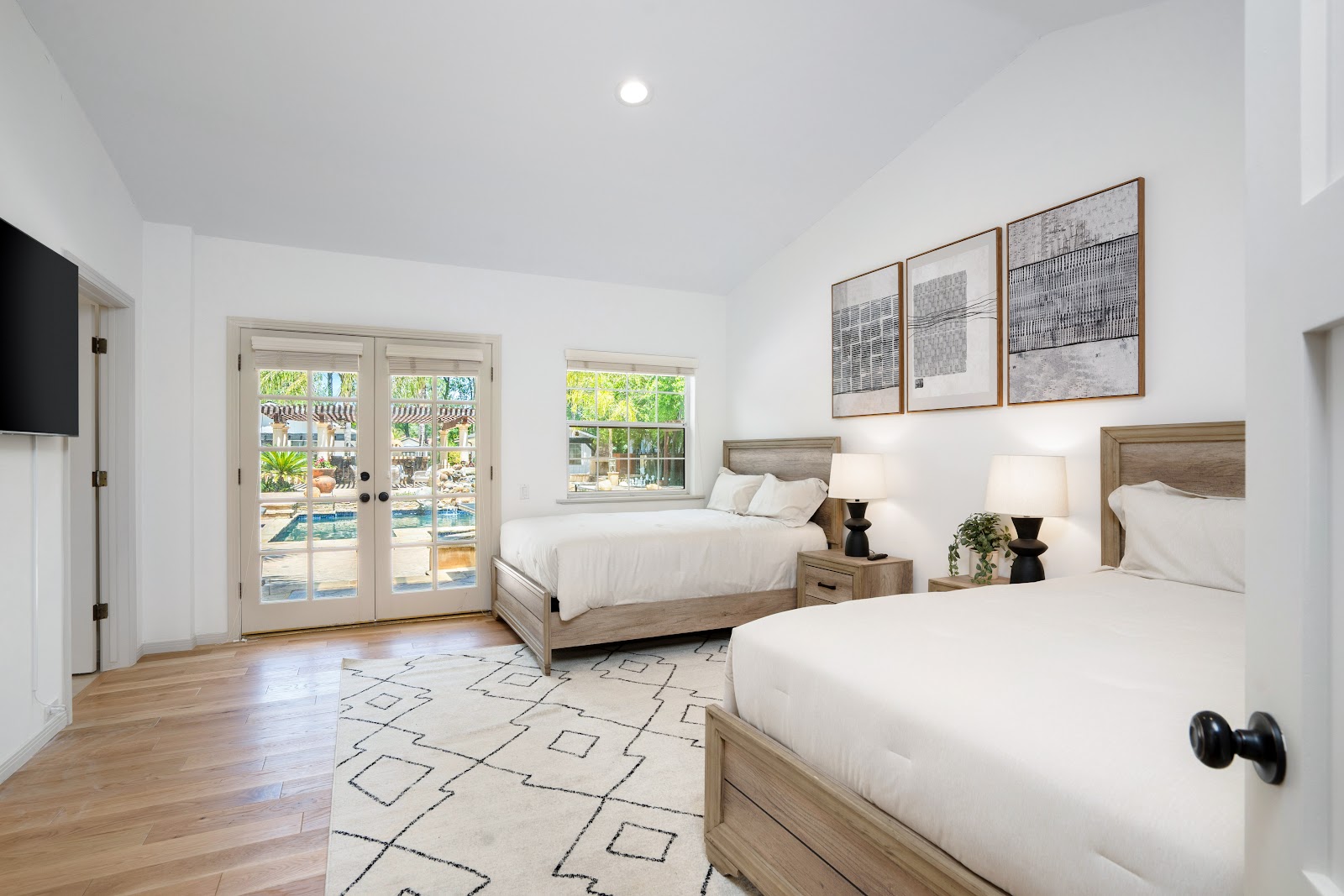 Interior guest bedroom with two beds, natural lighting from doors overlooking pool and landscaped grounds
