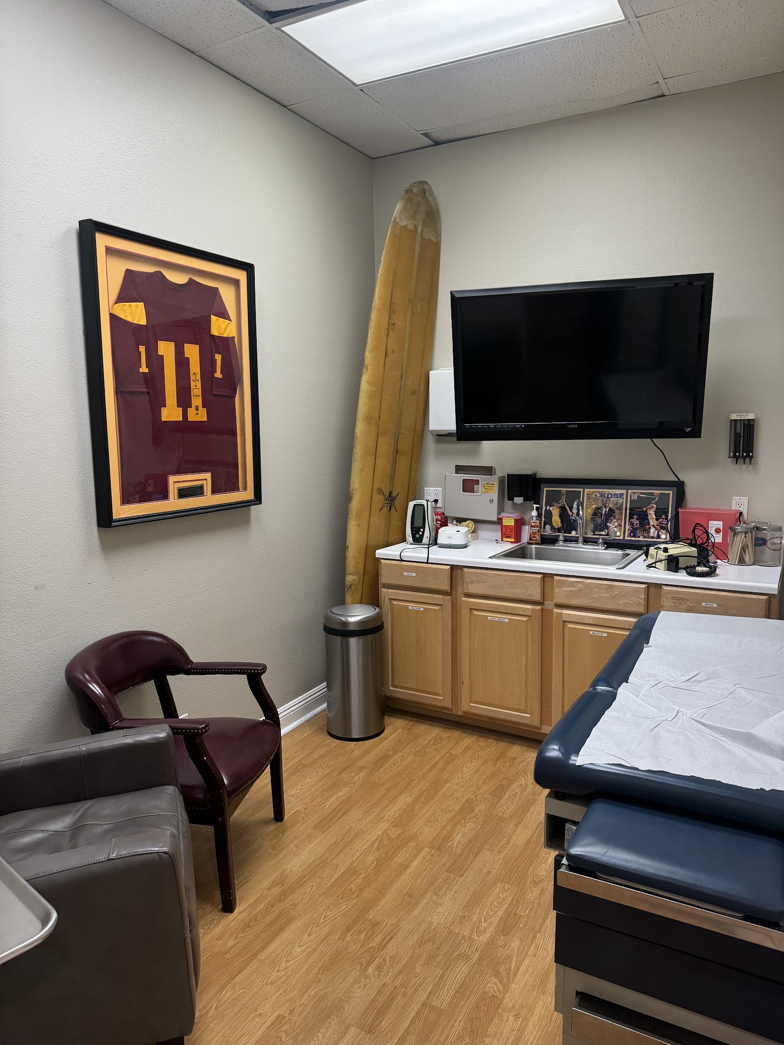 Interior patient bedroom featuring bed, television on wall, lounge seating, kitchenette with cabinets, and natural skylight