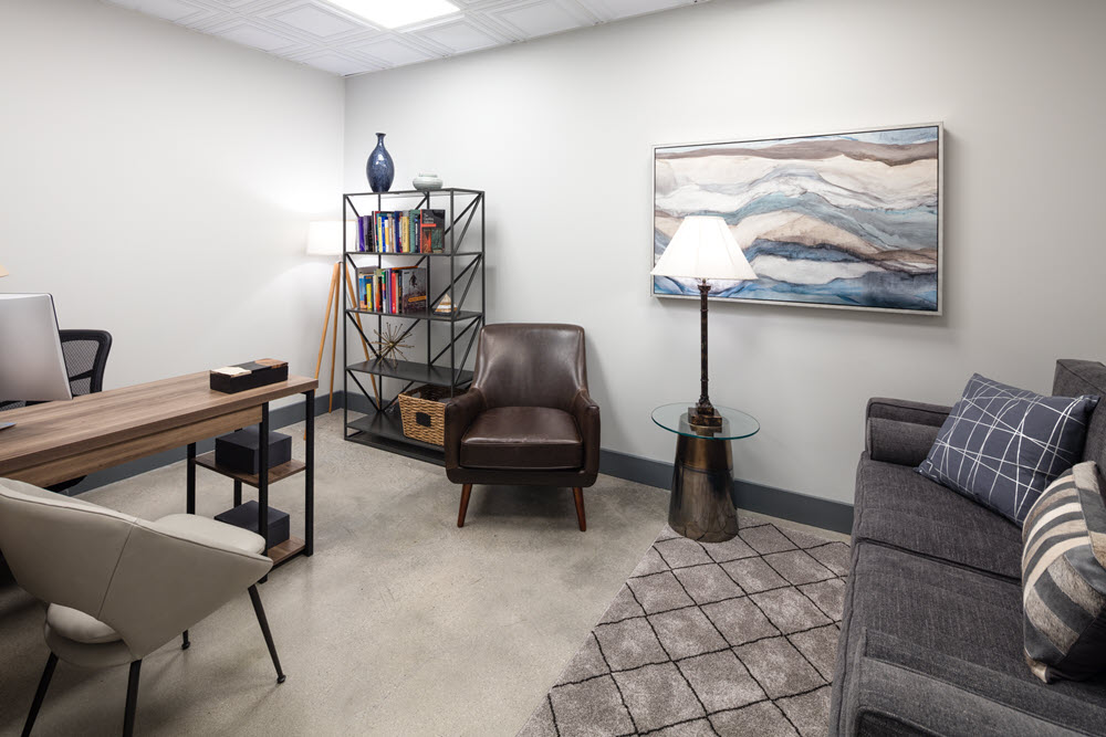 Interior office with desk, computer, leather chair, bookshelf, and framed wall art