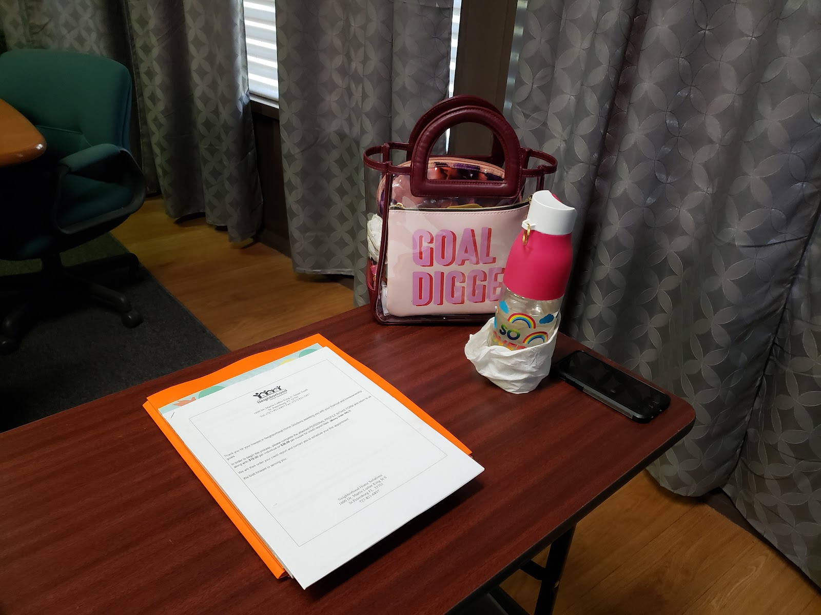 Interior private room with desk, orange folder with materials, water bottle, curtained windows, and comfortable seating