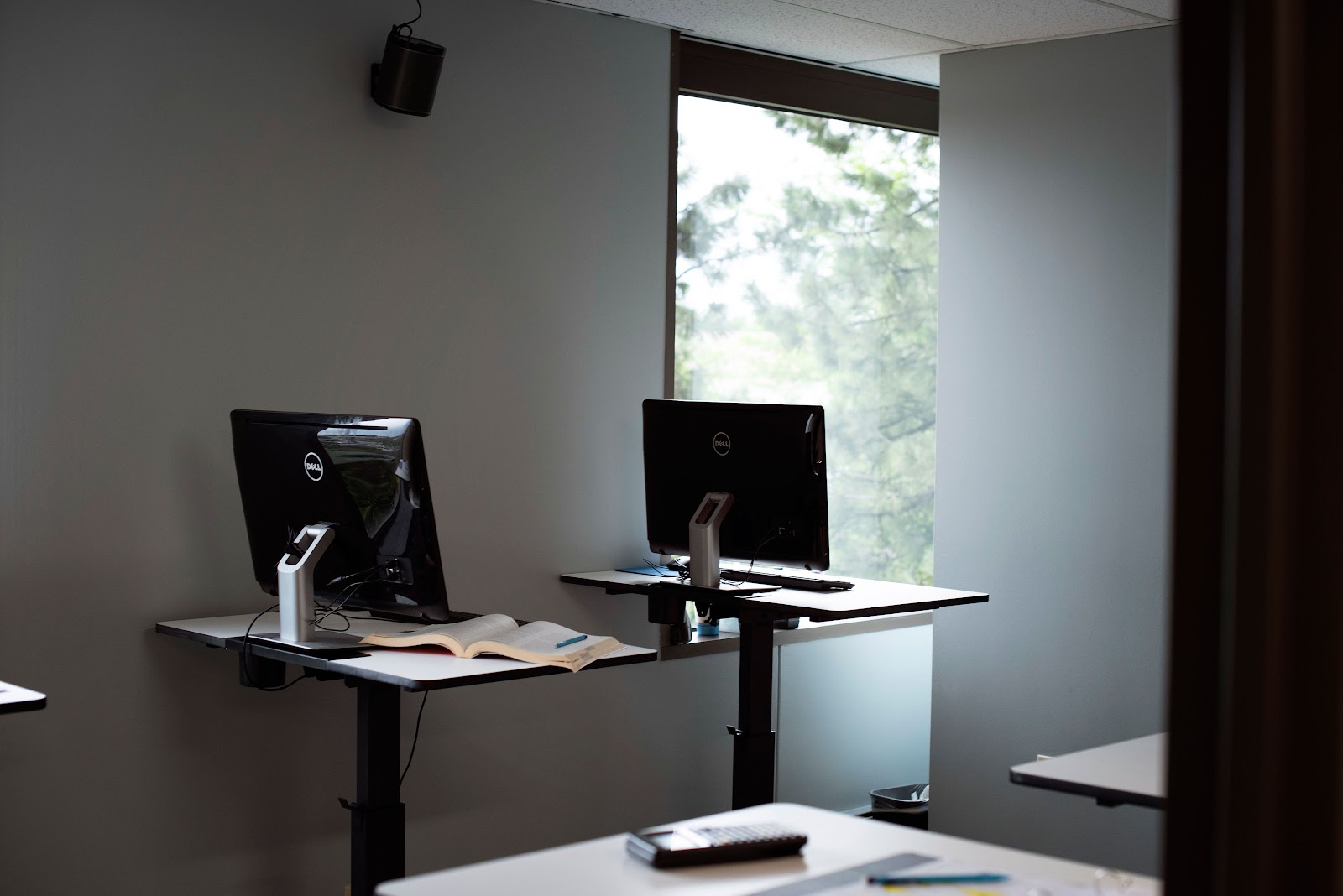 Interior office with desk-mounted Dell computer monitors, white desk surface, windows with natural light, and professional work environment