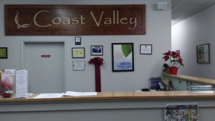 Interior reception area showing wooden front desk, Coast Valley facility signage, wall-mounted certifications, and office entrance
