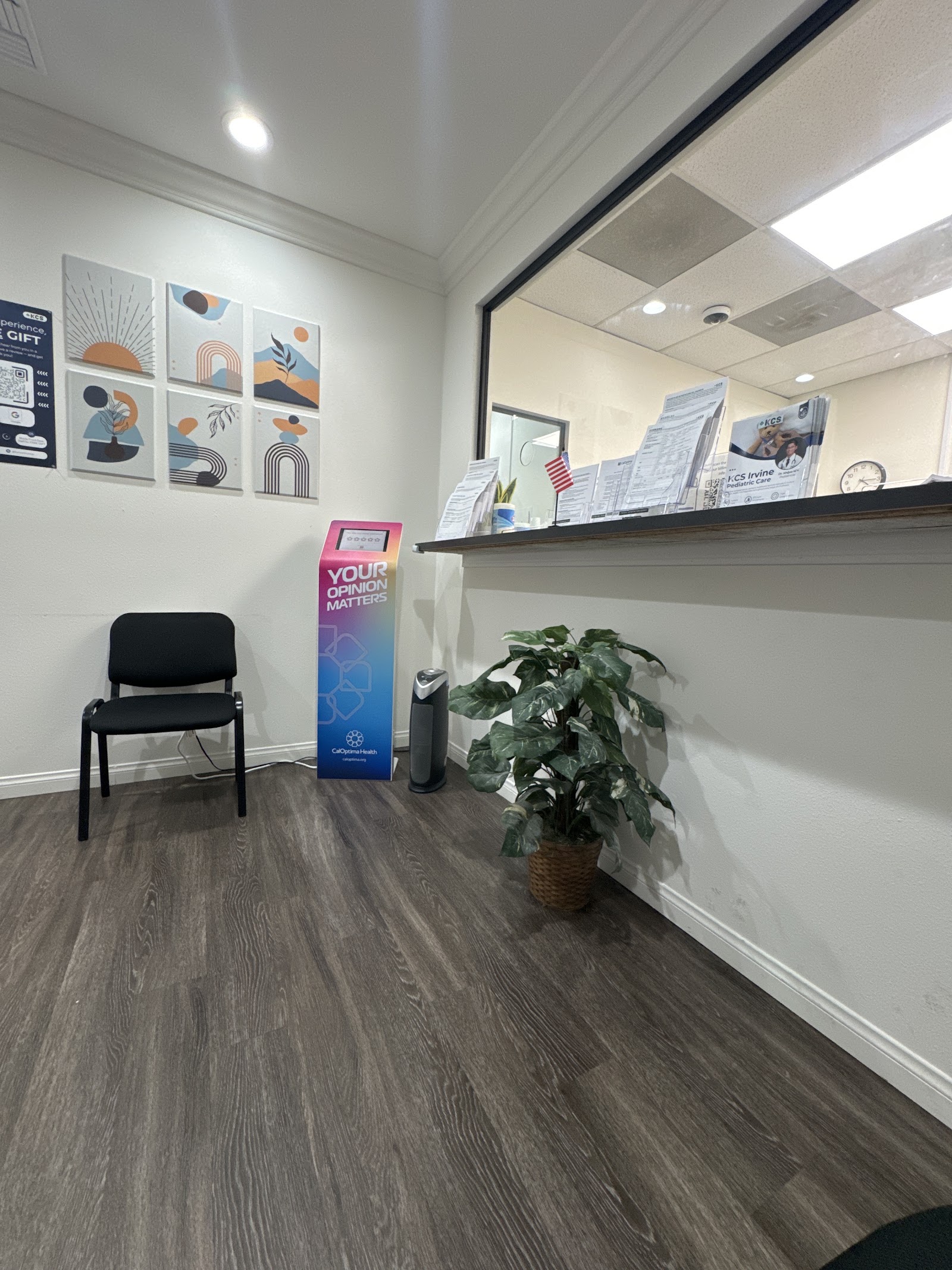 Interior waiting area with white walls, dark flooring, chair seating, potted plant, and abstract wall art displays