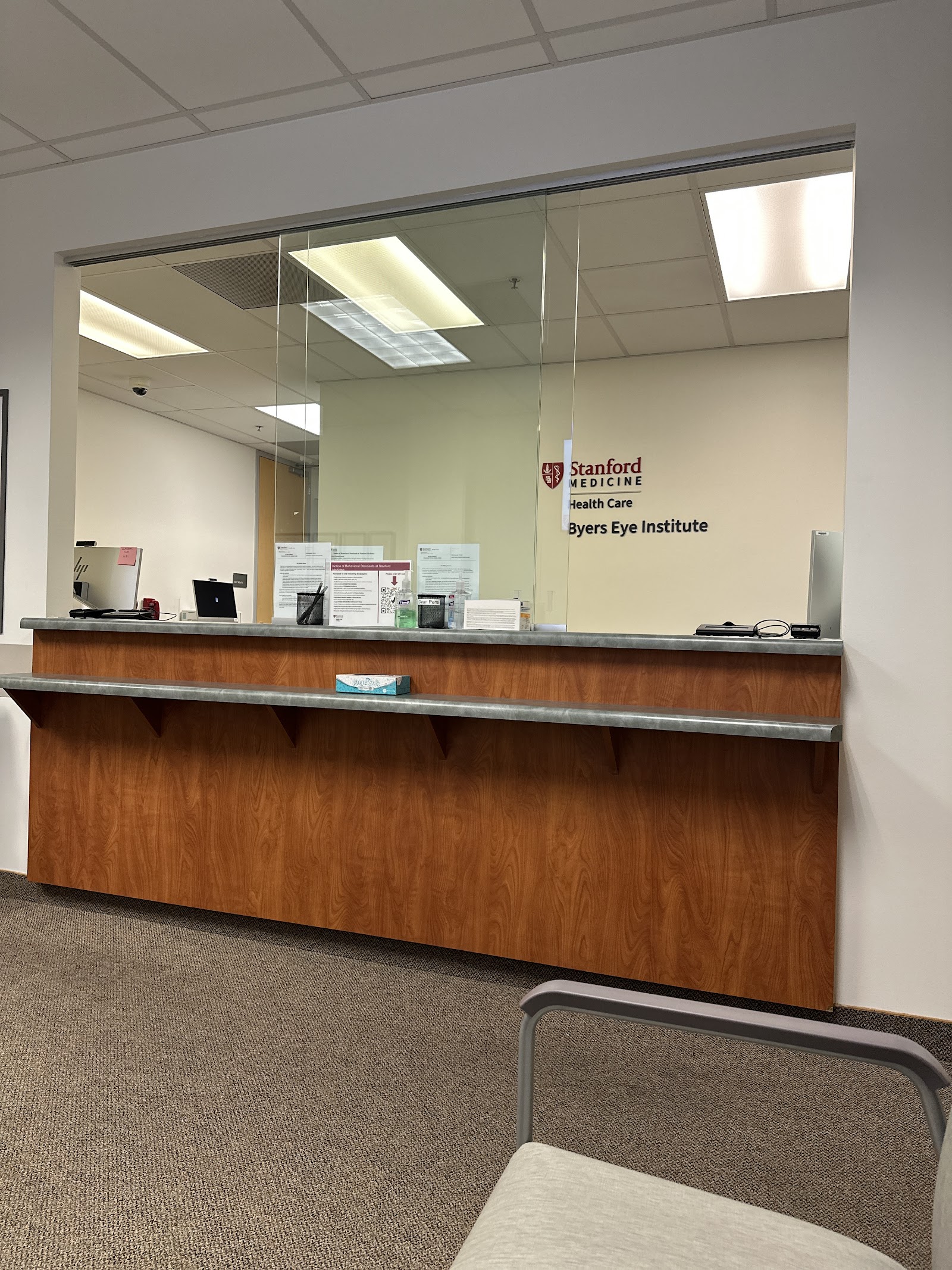 Interior reception desk area with glass partition, wooden counter, and facility signage for patient check-in