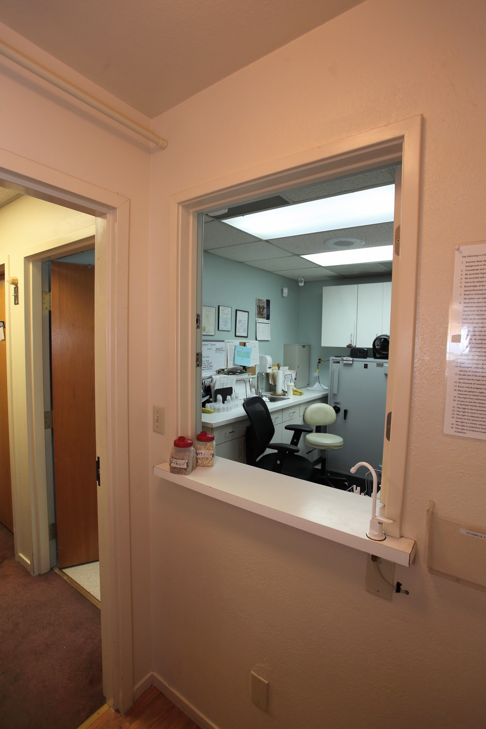 Interior reception area with pink walls, window counter, desk space with office supplies visible through glass separation