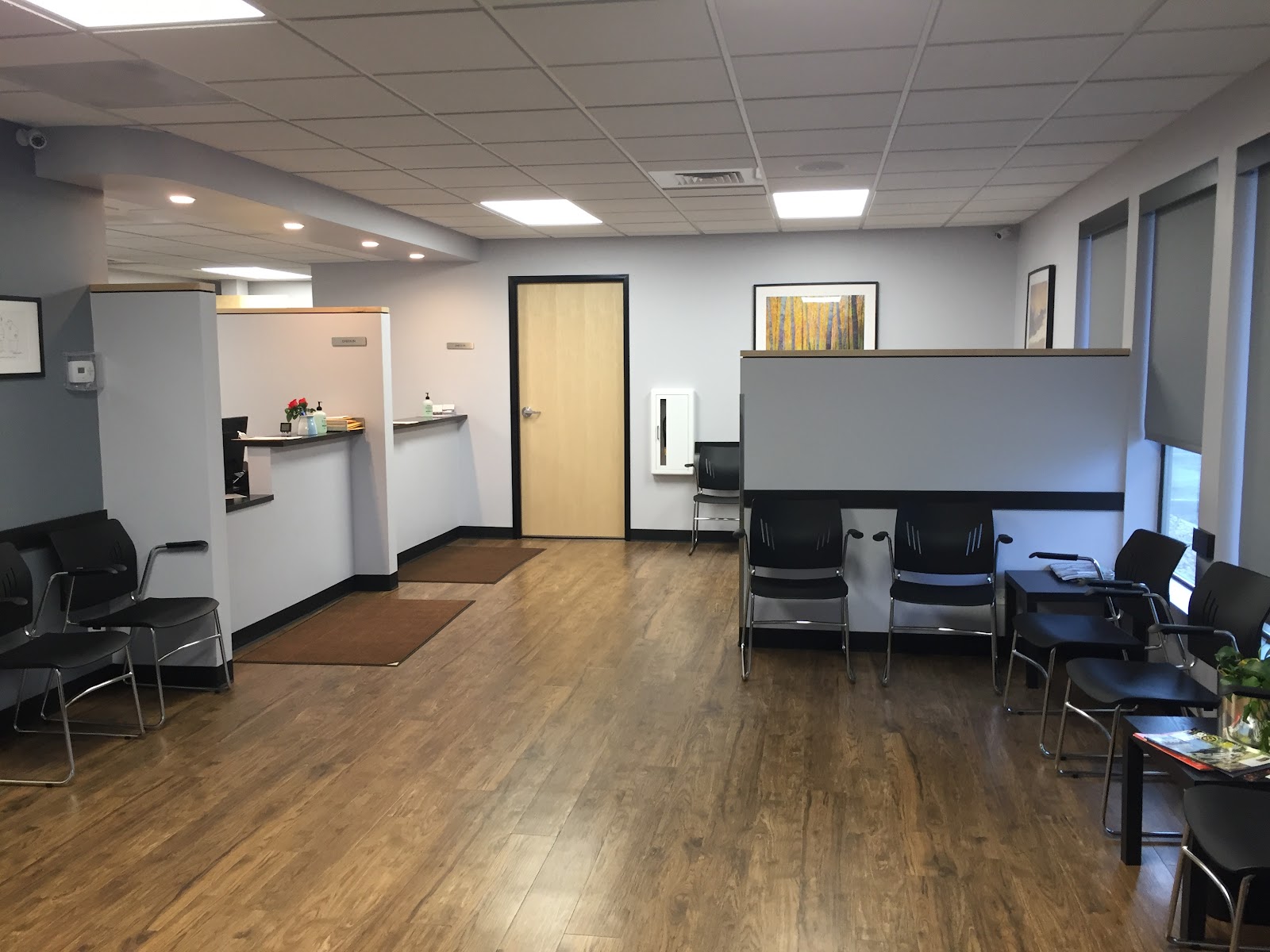 Interior reception area with check-in desk, waiting chairs, framed wall art, wood flooring, and doors leading to additional facility spaces