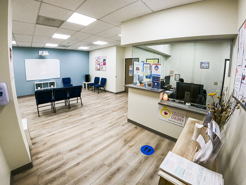 Interior reception space with light wood flooring, blue accent wall, reception desk, seating area, and posted informational materials