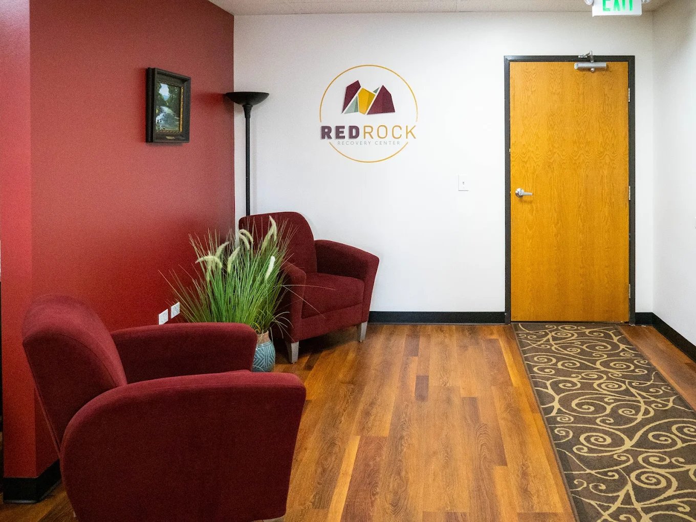 Interior reception lounge with red accent walls, comfortable seating, wooden furnishings, and facility branding