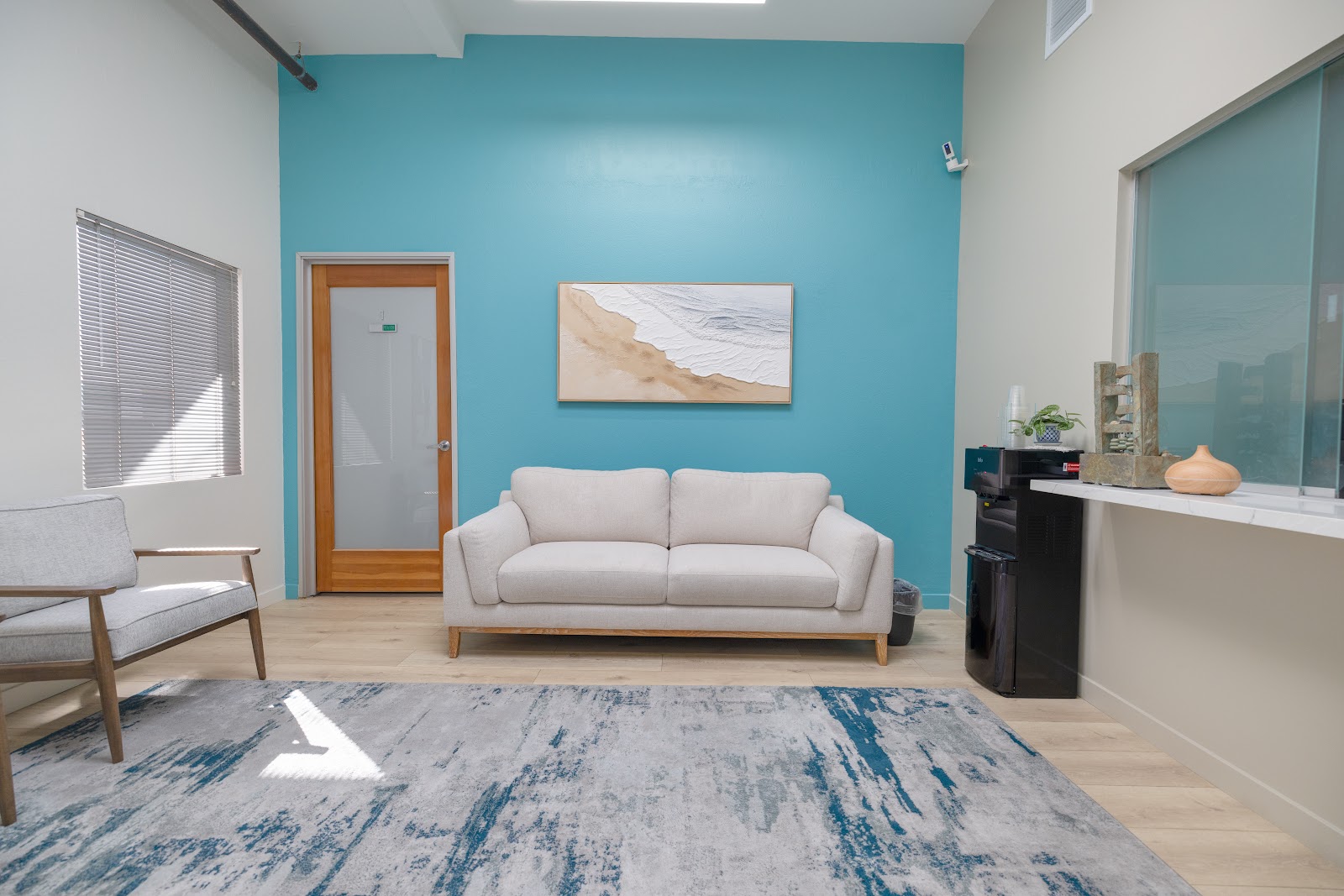 Interior reception area with turquoise accent wall, beige sofa, wooden door, and beach-themed artwork on walls