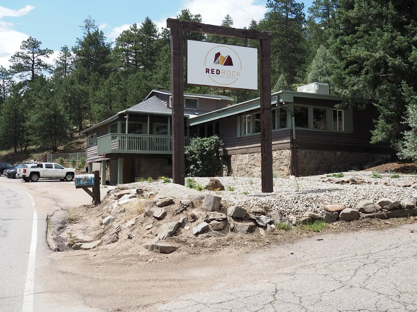 Exterior mountain facility with covered porch, parking area, wooden signage, and forested surroundings
