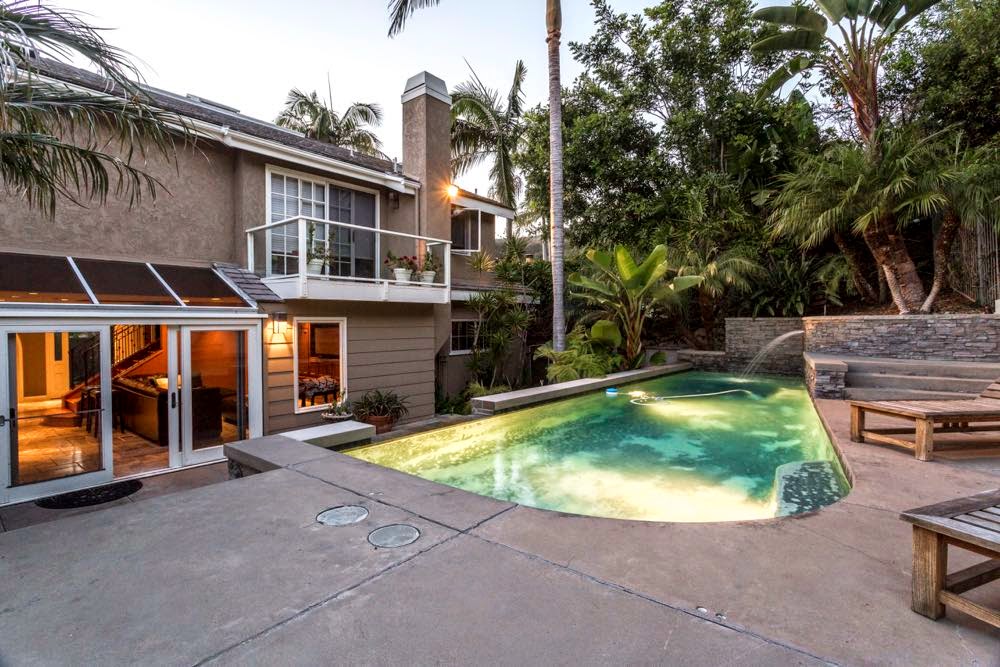Illuminated swimming pool with lounge seating, stone walls, palm trees, and modern residential patio design