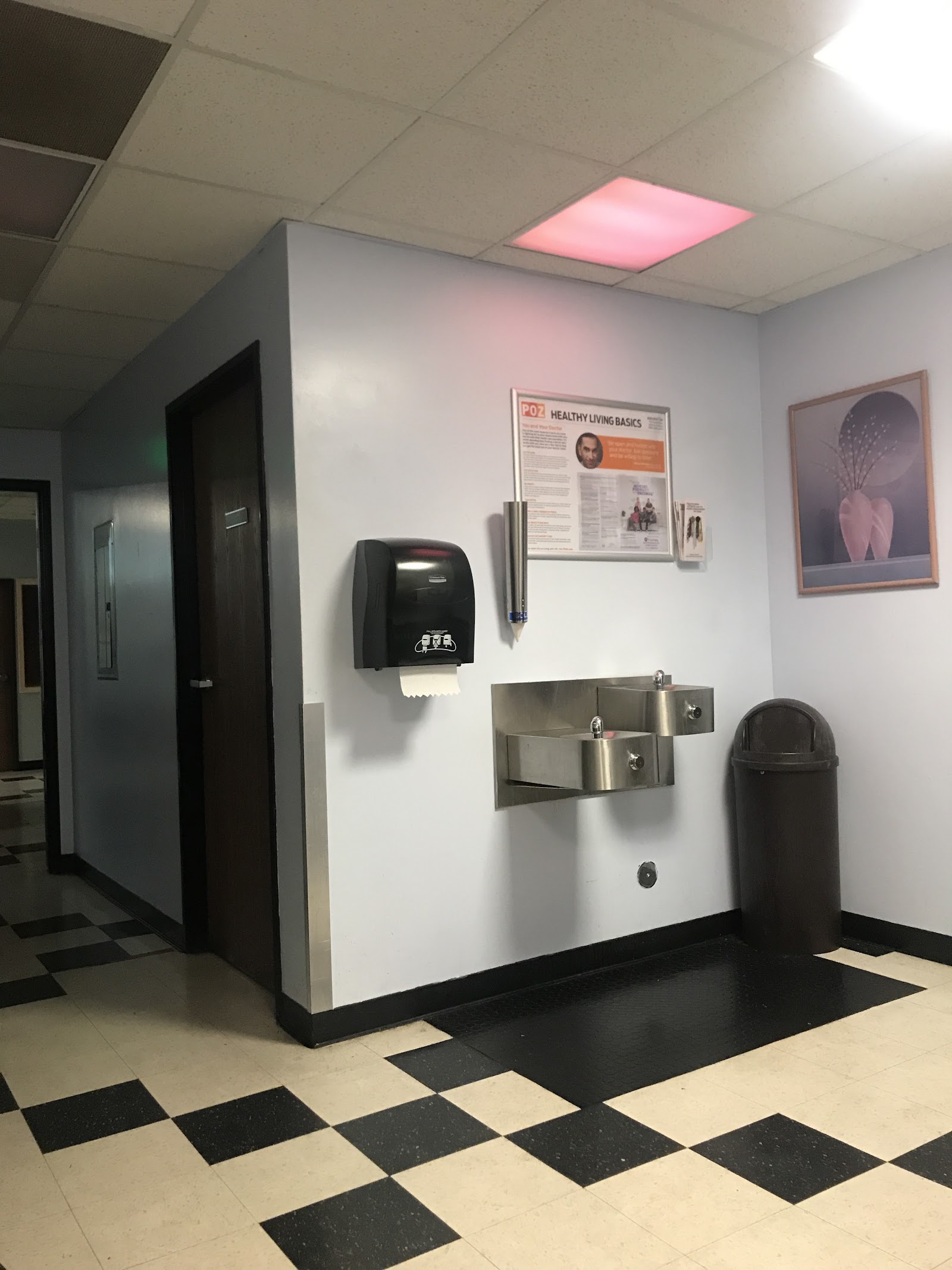 Interior restroom featuring wall-mounted paper towel dispenser, soap dispenser, trash bin, and educational signage on light blue wall