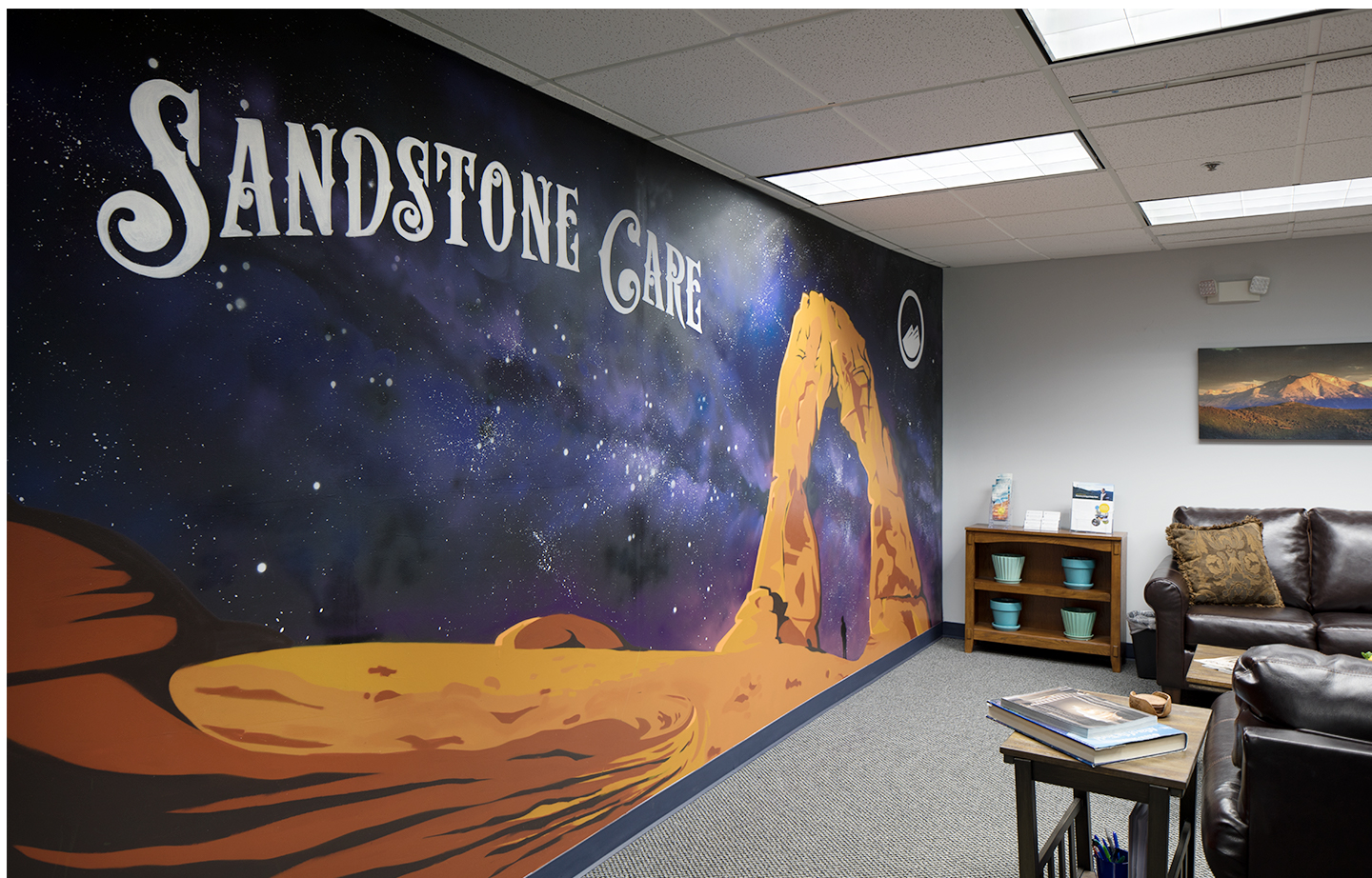 Interior wall featuring desert-themed mural with Sandstone Care logo, astronauts, and rock formations in orange and purple tones