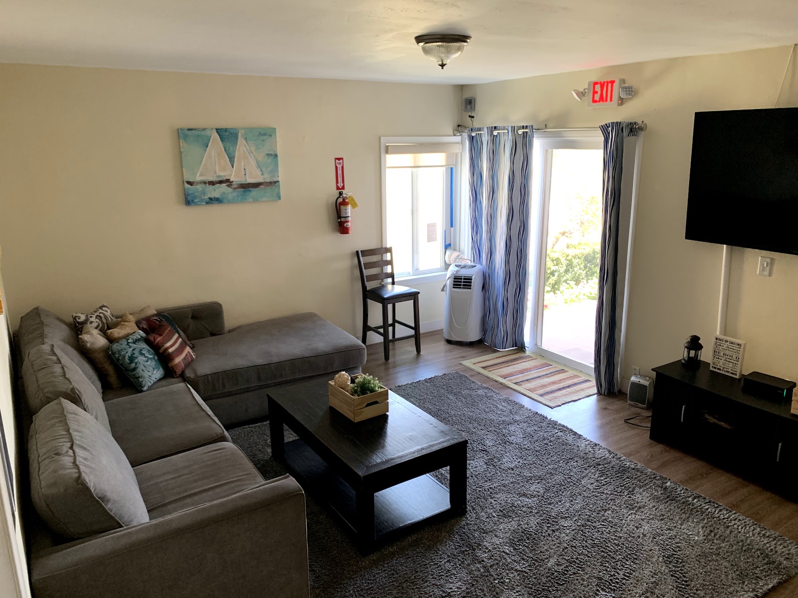 Interior lounge space with gray sectional sofa, sailboat painting, fire extinguisher, and patio access