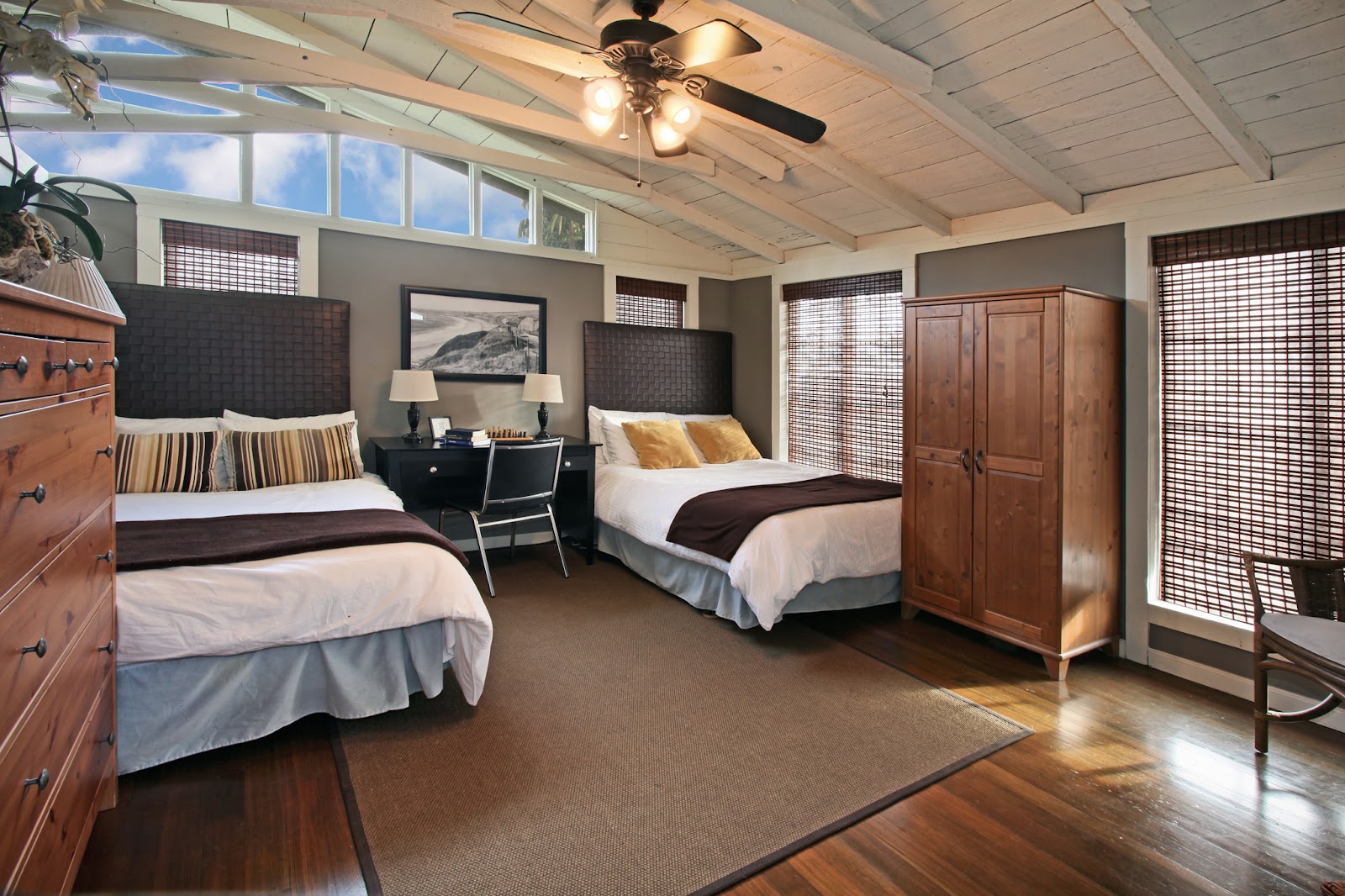 Interior bedroom with two twin beds, dark headboards, desk area, and large windows with privacy screens
