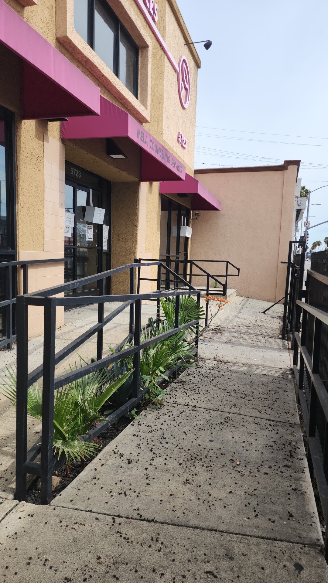 Exterior side walkway with metal railings, planted greenery, and access path to facility entrance