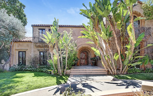 Exterior view of Spanish colonial-style building with tan walls, arched entryway, and desert landscaping with cacti