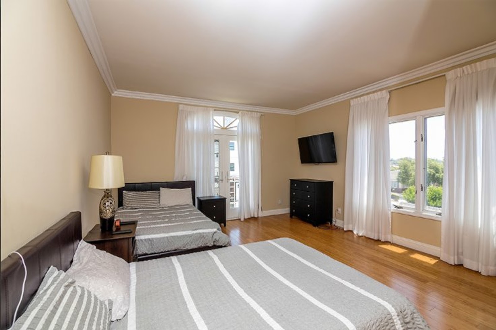 Interior bedroom suite with two beds featuring striped bedding, black dressers, flat-screen TV, and large windows