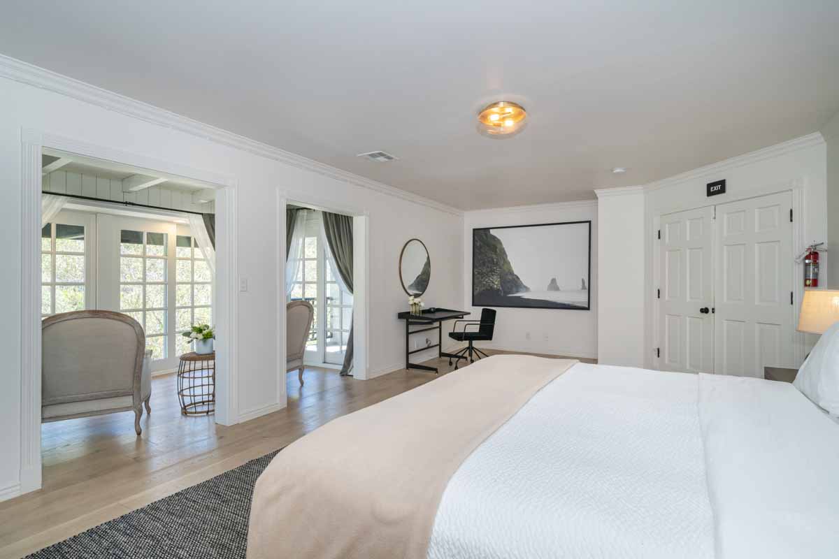 Interior bedroom with king bed, workspace with desk, seating area, and French doors to outdoor patio