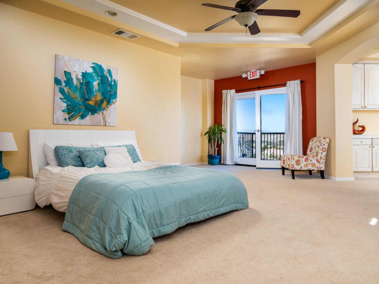 Interior master bedroom with queen bed, sitting area, balcony doors, and panoramic window views