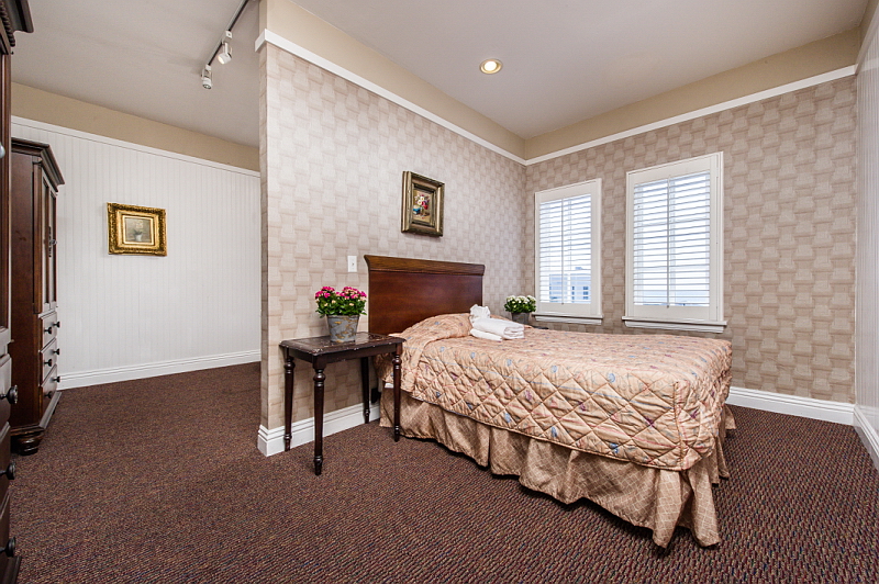Interior bedroom with queen bed, side table with flowers, white shutters, carpeted flooring, framed wall art, and modern furnishings