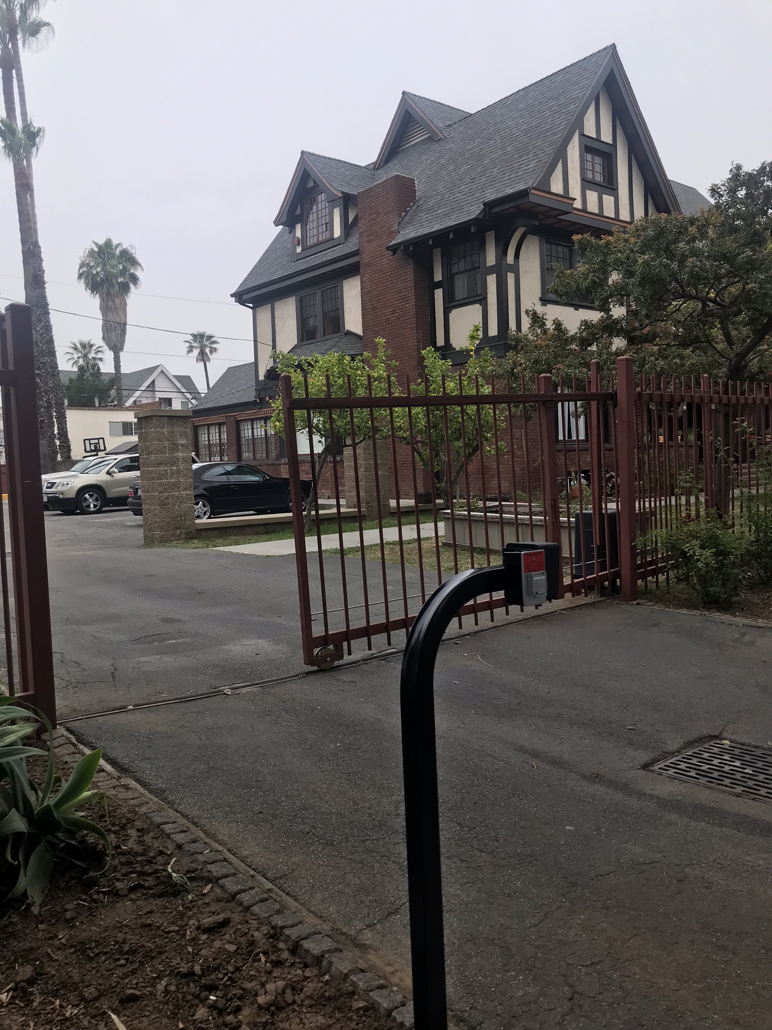 Street-level exterior view of two-story brick building with security gate, residential setting, and mature landscaping
