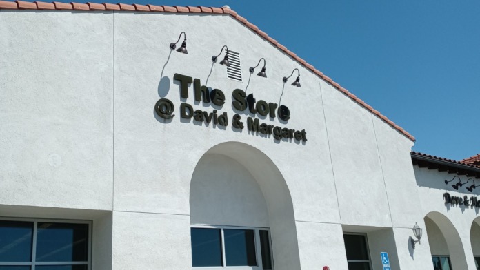 Exterior storefront with white facade, arched entrance, signage, large windows, and parking area