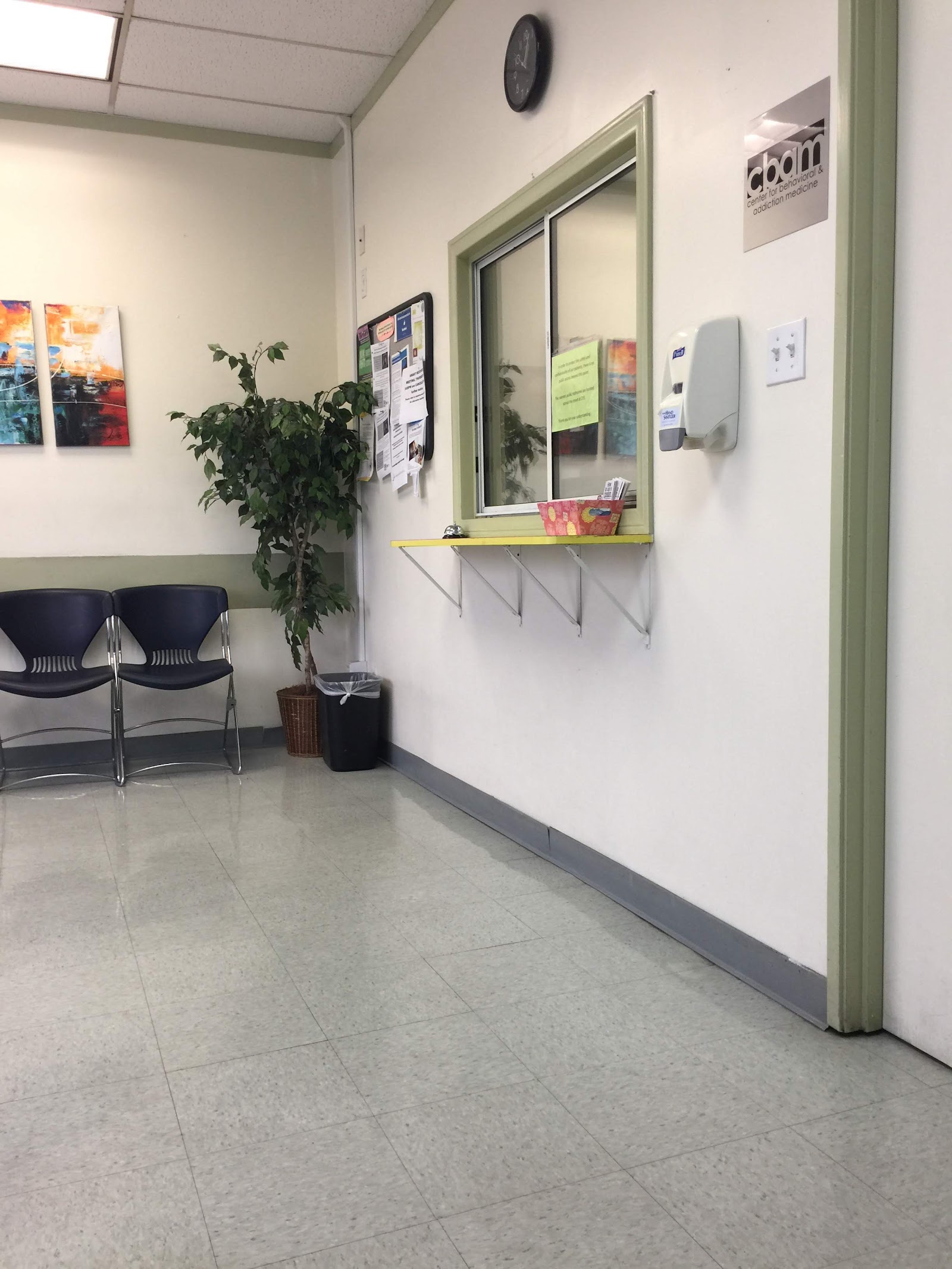 Interior waiting area with reception window, blue chairs, plants, and wall displays