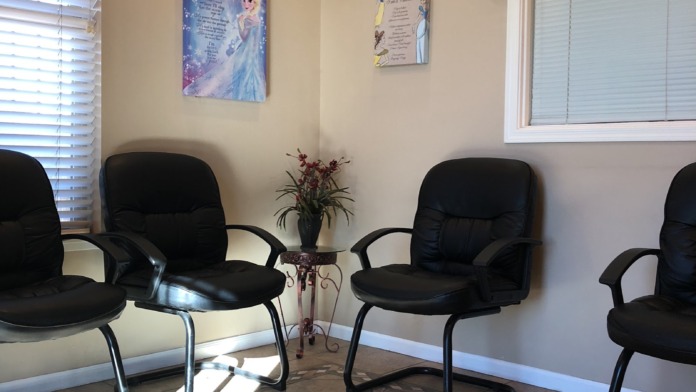 Interior waiting room featuring black cushioned chairs arranged in conversation groupings, large windows with blinds, and decorative wall art