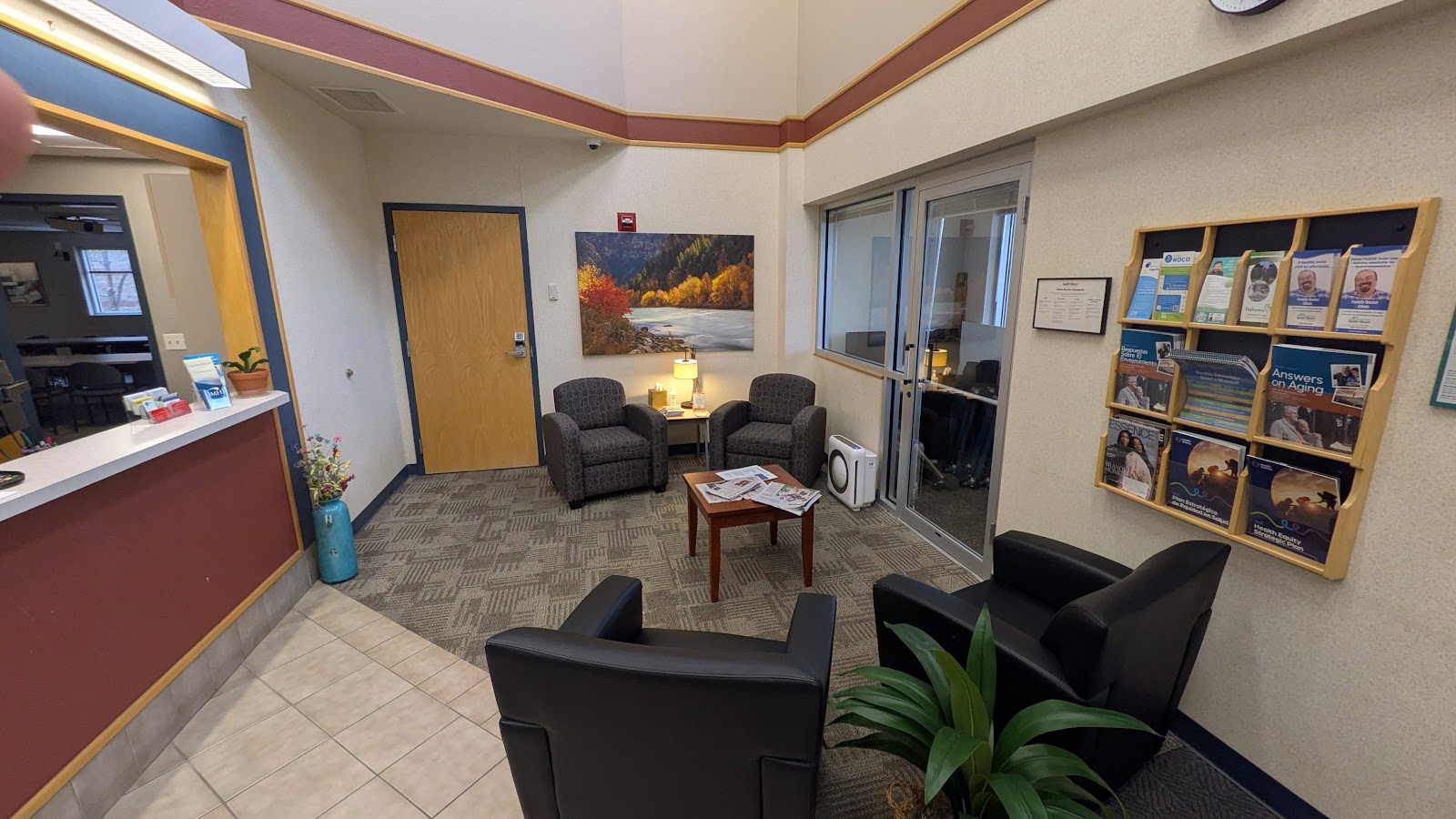 Interior reception and waiting space with black seating chairs, burgundy desk counter, landscape artwork, and resource display shelving