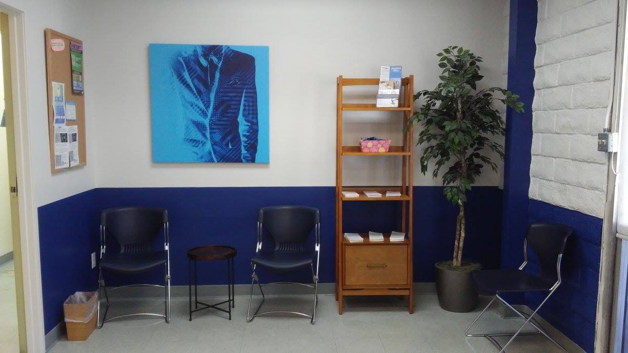 Interior waiting area with blue accent wall, chairs, wooden shelving with brochures, and plants