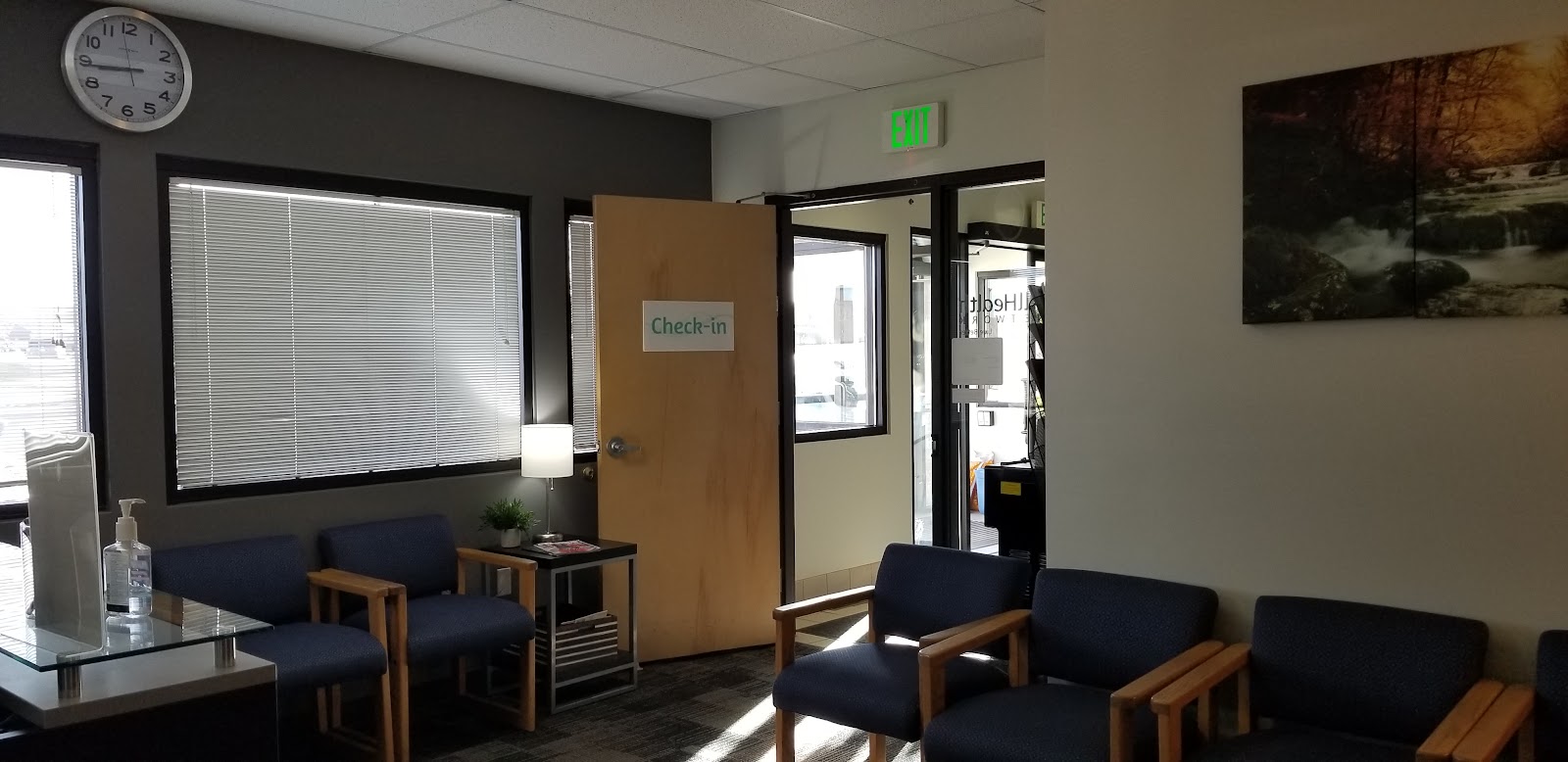 Interior waiting area with blue upholstered seating, exit sign, and natural lighting from windows