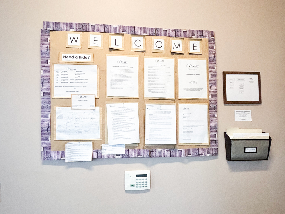 Interior wall display with purple-framed welcome board containing informational documents and resource materials for clients