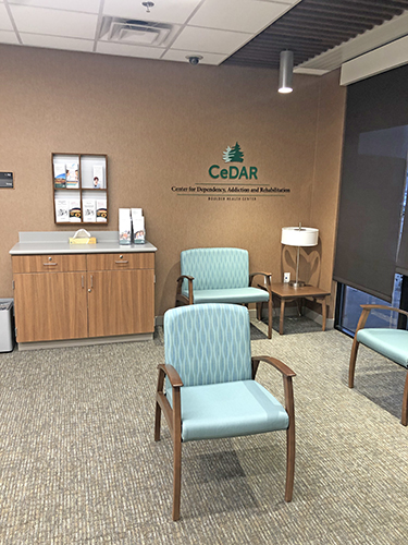Interior lobby space with light blue upholstered chairs, wooden storage cabinet, and CeDAR facility signage on wall