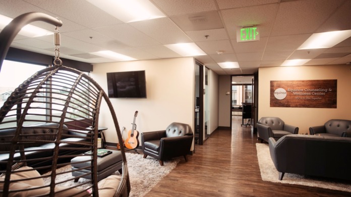 Interior reception area with woven chair seating, guitar, leather armchairs, wooden flooring, and facility signage on brick wall