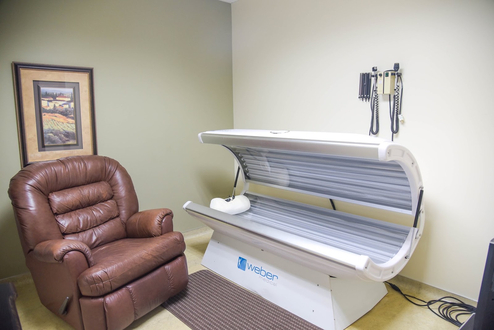 Interior spa treatment room with tanning bed, leather recliner, framed artwork, and neutral colored walls