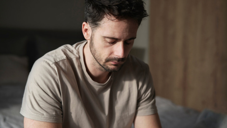 A depressed man sitting pensively. Lean more about the signs, risks, and treatment for opioid addiction here.